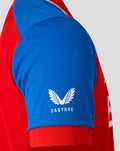 Close-up of blue sleeve with white Castore logo and wing emblem on a red England cricket jersey.