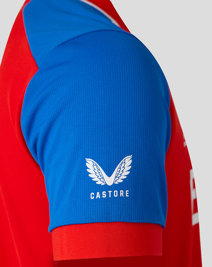 Close-up of blue sleeve with white Castore logo and wing emblem on a red England cricket jersey.