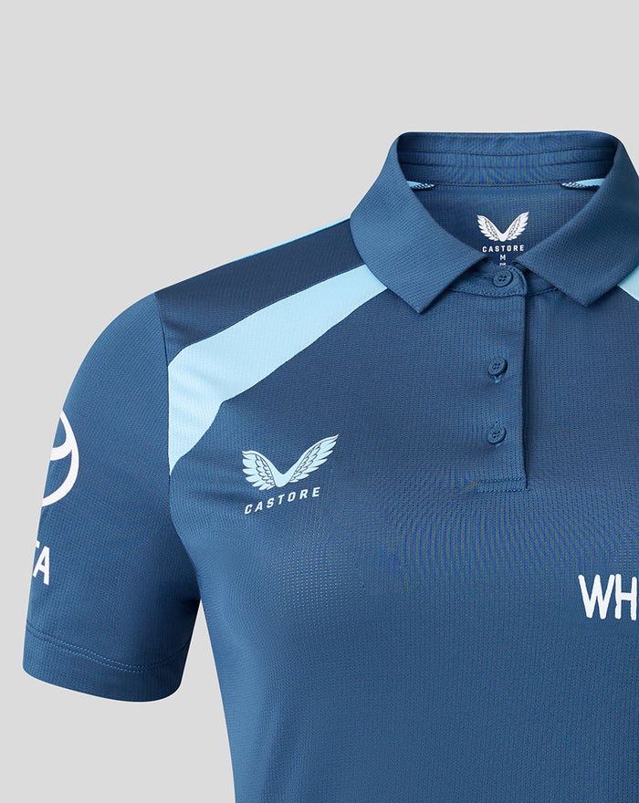 Close-up of the polo chest showing Castore branding and navy England crest on blue fabric.