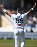 Cricketer wearing a white England Test short sleeve shirt seen from behind with arms raised.