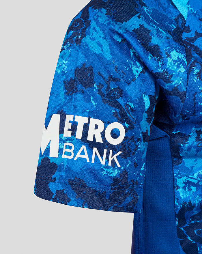 Close-up of sleeve featuring Metro Bank logo on blue camouflage England cricket shirt.