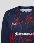 Close up of navy junior long sleeve shirt showing red geometric print and Lancashire Cricket crest with Sportsbreaks logo