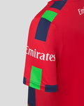 Shoulder close-up of red junior T20 jersey featuring Emirates sponsor and navy trim.