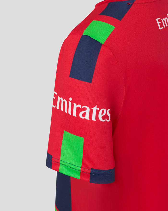 Shoulder close-up of red junior T20 jersey featuring Emirates sponsor and navy trim.