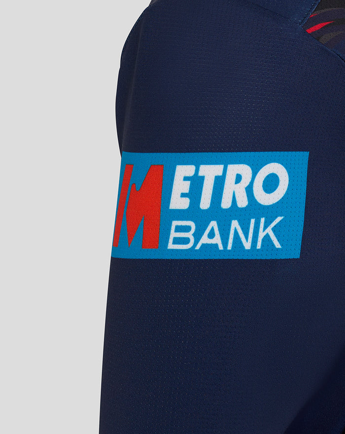 Close-up of left sleeve showing a bright Metro Bank patch on the navy long sleeve jersey.