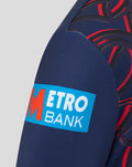Close up of navy sweatshirt sleeve with blue Metro Bank patch and red graphic print.