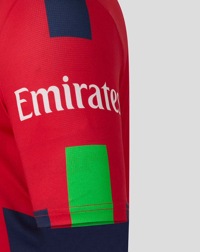 Close-up of a red T20 cricket jersey with Emirates sponsor across the chest and bold blue and lime graphic blocks on the sleeve.