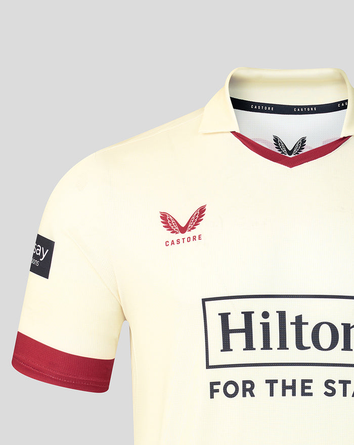 Chest close-up of cream Lancashire County Championship jersey showing red rose crest and Hilton sponsor with Castore collar detail.